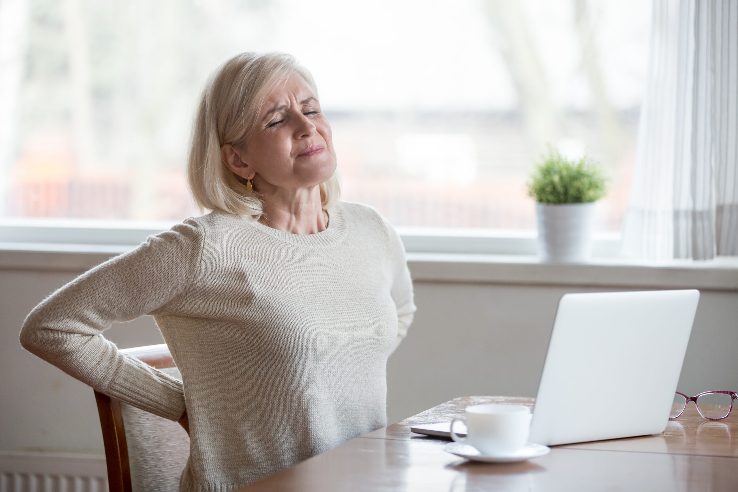 Older woman experiencing back pain while sitting at a table