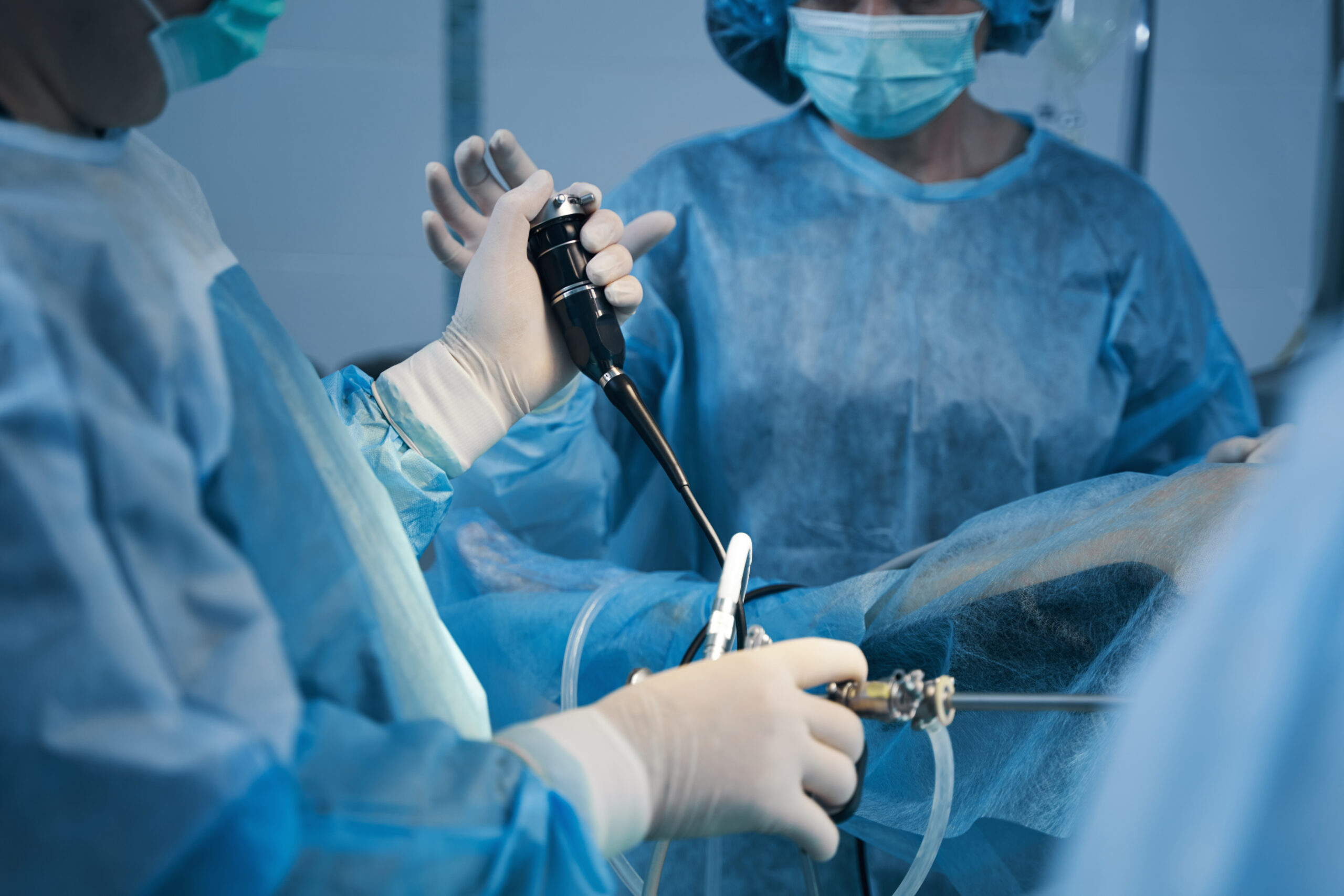 Cropped photo of two doctors in surgical gowns standing near the patient and using hysteroscope