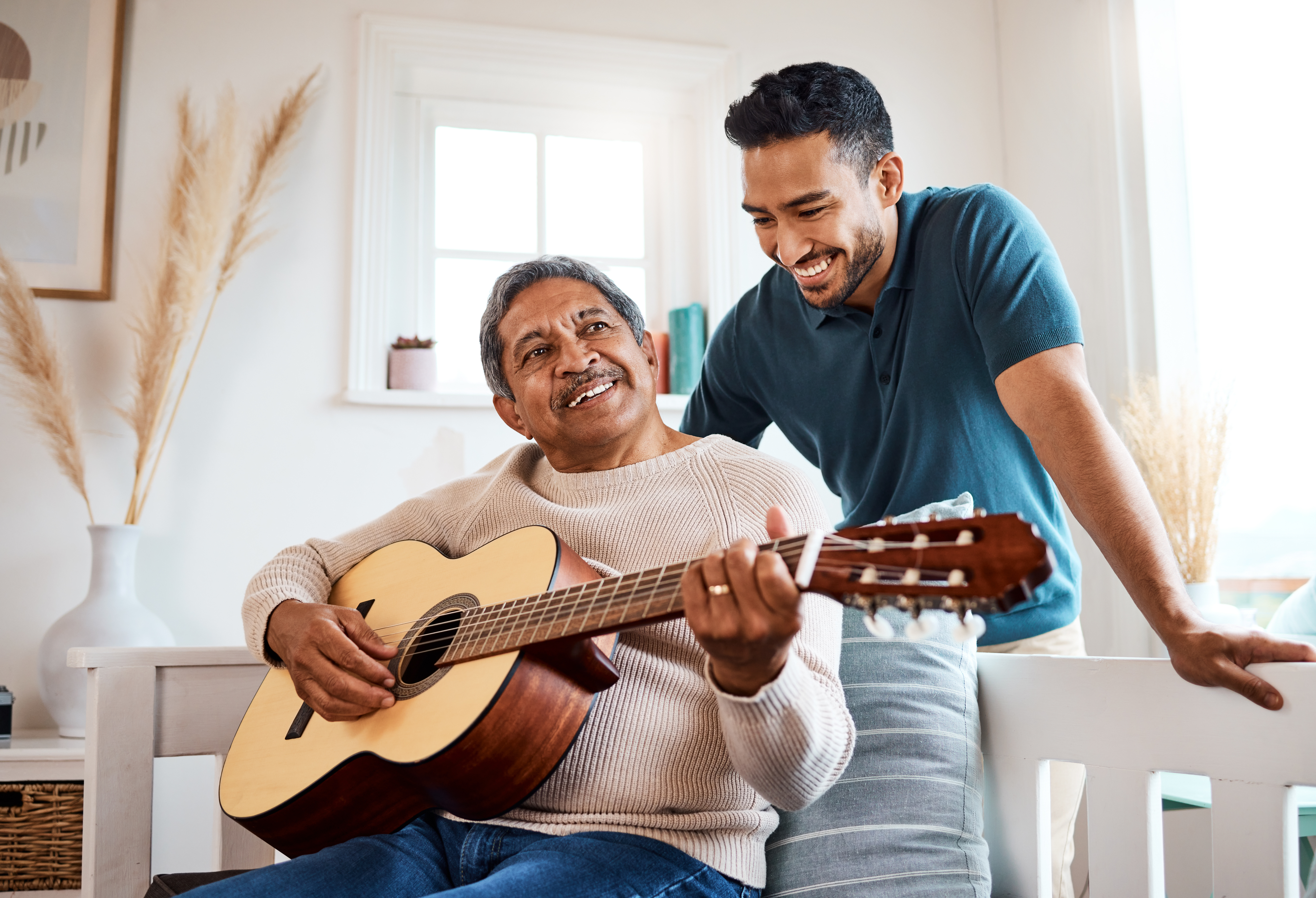 Shot of a young man listening to his father play the guitar at home.